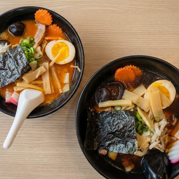 Two bowls of ramen topped with seaweed, soft-boiled eggs, bamboo shoots, mushrooms, carrots, scallions, and fish cakes.