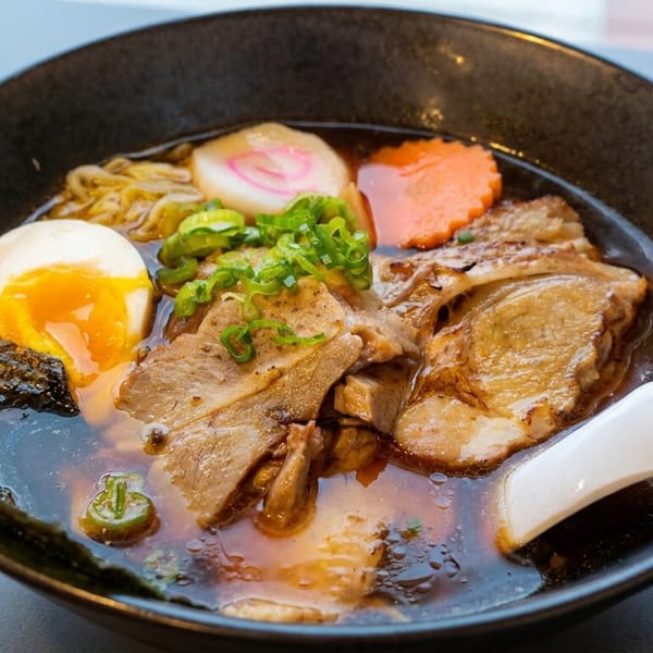 Bowl of Japanese ramen with pork slices, soft-boiled egg, seaweed, green onions, fish cake, and vegetables in broth.